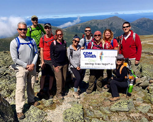 10 CDM Smith employees in hiking hear at the top of a mountain with a check for Water For People