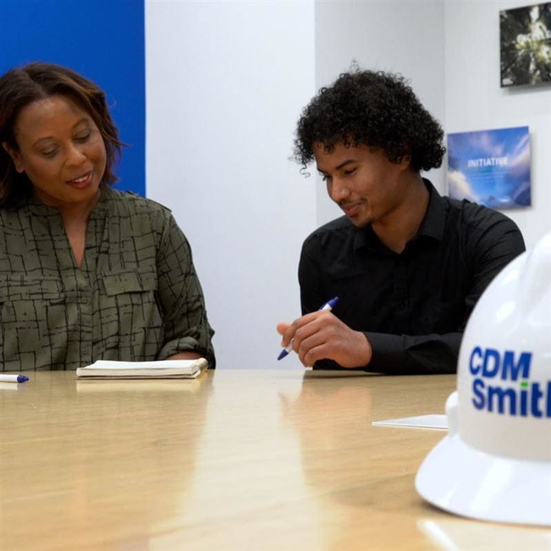 two people at a table with hard hat in front