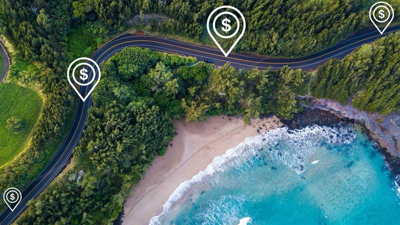 An aerial view of a highway in Hawaii, with illustrations of dollar signs conveying road usage charges.